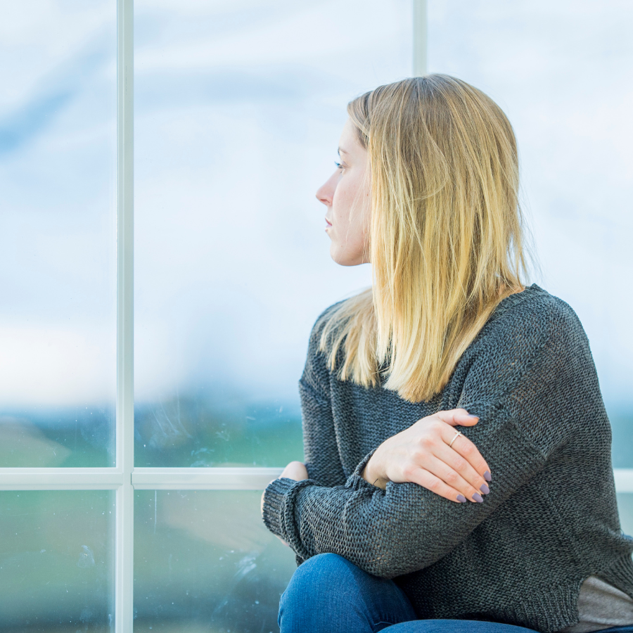 Woman staring pensively out of a window at a cloudy sky. 